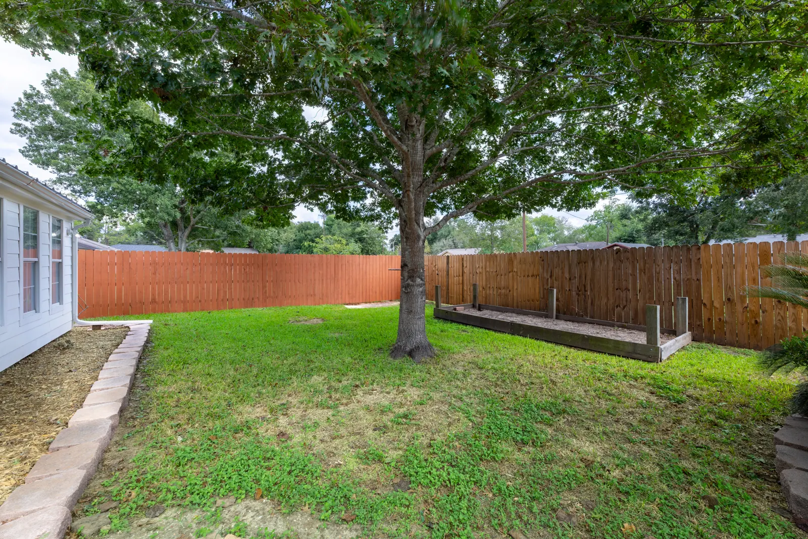 Fenced backyard with a large shade tree