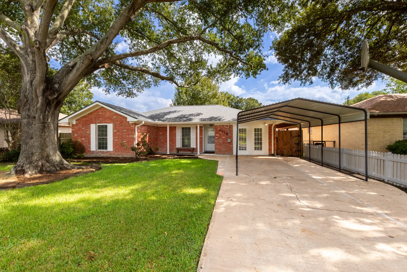 Front of 3419 Beasley Avenue: red brick single-story home with a covered carport and a large oak tree in the front yard