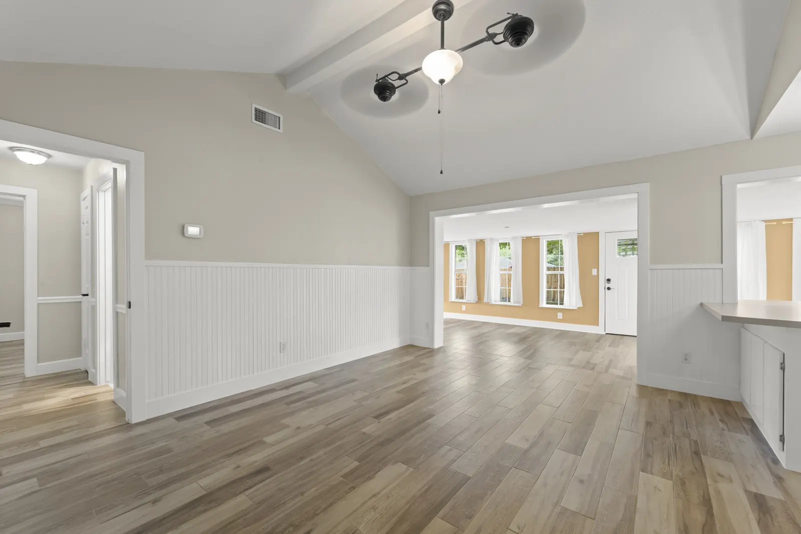 Living room with wood-look floors, wainscoting and a vaulted beamed ceiling